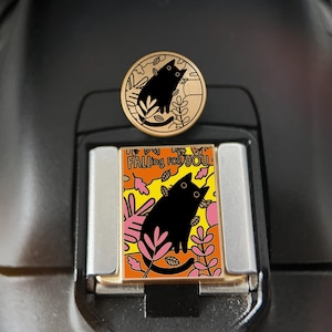 Puede incluir: Dos pines de esmalte con temática de gatos. Uno es redondo con un gato negro y hojas sobre un fondo dorado. El otro es rectangular con un gato negro, hojas y el texto "Falling for You" sobre un fondo amarillo y naranja.