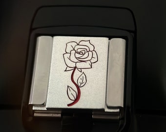 May include: A silver-colored square tile with a red and white rose design. The rose is outlined in black and has a red stem and leaves.