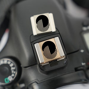 以下が含まれることがあります： カメラ用の白黒のフラッシュディフューザー2つ。ディフューザーはカメラのホットシューに取り付けられています。