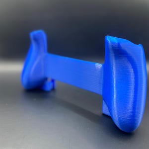 May include: A vibrant blue game controller grip, designed for enhanced ergonomics. The device features two rounded handles connected by a central bar. The textured surface suggests a 3D-printed construction, offering a comfortable hold for extended gaming sessions.