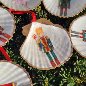 May include: A set of six white seashells with gold trim, each decorated with a different image from the Nutcracker ballet. The images include a ballerina, a nutcracker soldier, and a candy cane.