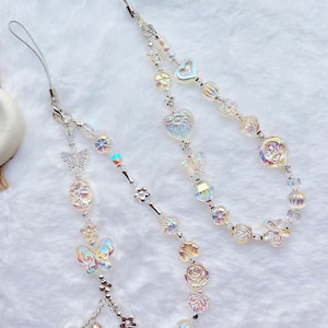 May include: Two iridescent phone charms with silver chains and various charms, including butterflies, hearts, flowers, and leaves.