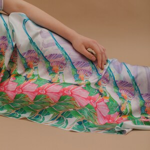 May include: A white silk dress with a colorful floral print featuring pink flowers, green leaves, and purple and blue accents. The dress has a flowing, relaxed fit.