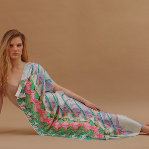 May include: A woman wearing a light blue and white patterned silk scarf with pink and green floral accents. The scarf is draped over her shoulders and around her waist.