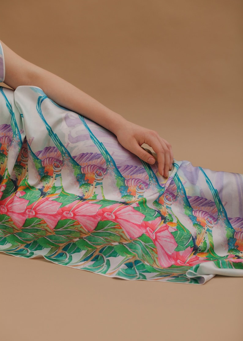 May include: A white silk dress with a colorful floral print featuring pink flowers, green leaves, and purple and blue accents. The dress has a flowing, relaxed fit.
