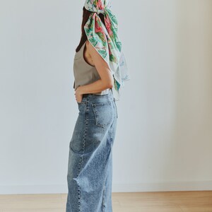 May include: A woman wearing a light gray sleeveless vest, a long denim skirt, and a floral patterned headscarf.