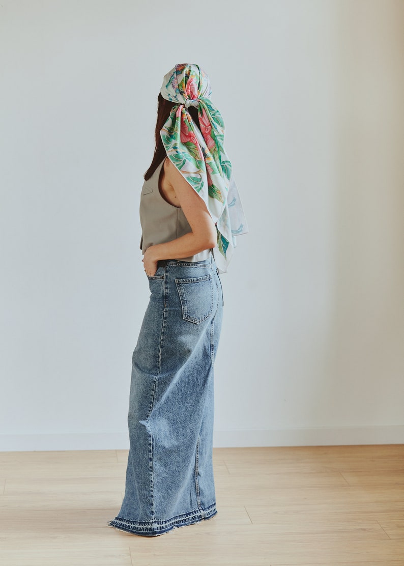 May include: A woman wearing a light gray sleeveless vest, a long denim skirt, and a floral patterned headscarf.