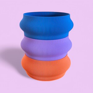 May include: A three-tiered planter with a blue, purple, and orange colour scheme. Each tier has a wavy, ribbed design.