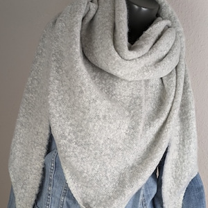 Könnte beinhalten: Ein grauer Strick Schal mit weicher, flauschiger Textur. Der Schal ist über eine Jeansjacke gelegt.