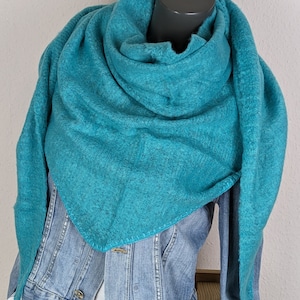 Könnte beinhalten: Ein türkisfarbener, dreieckiger Schal, der über einer Jeansjacke drapiert ist. Der Schal besteht aus einem weichen, strukturierten Material und ist um den Hals einer Schaufensterpuppe gewickelt. Die Jeansjacke ist hellblau und hat ein klassisches Design.