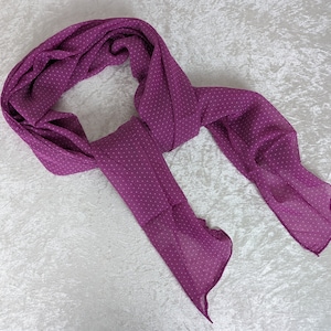 Può includere: Una sciarpa viola con pois bianchi. La sciarpa è realizzata in un tessuto morbido e trasparente ed è piegata a metà.
