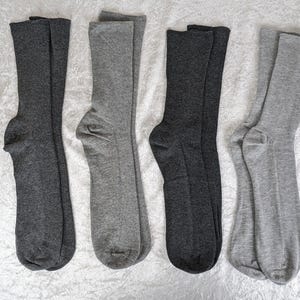 Könnte beinhalten: Vier Paar Socken, zwei Paar sind grau und zwei Paar sind schwarz. Die Socken sind gefaltet und auf einer weißen Oberfläche ausgelegt.
