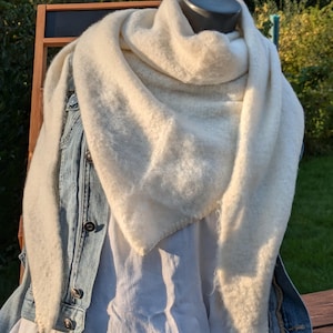 Könnte beinhalten: Ein weißer, flauschiger Schal, der über eine Jeansjacke und ein weißes Hemd gelegt wird. Der Schal ist aus einem weichen, strukturierten Material gefertigt und hat eine dreieckige Form.