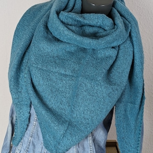 Könnte beinhalten: Ein tealblauer Strick Schal mit weicher, flauschiger Textur. Der Schal ist gefaltet und um den Hals einer Schaufensterpuppe gelegt.