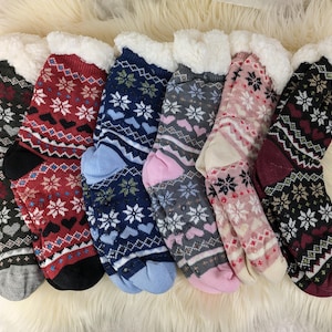 Può includere: Una collezione di sei paia di calzini caldi e fantasia con finiture in ecopelliccia bianca. I calzini presentano disegni a fiocco di neve, a cuore e geometrici in vari colori, tra cui grigio, rosso, blu, rosa e nero.