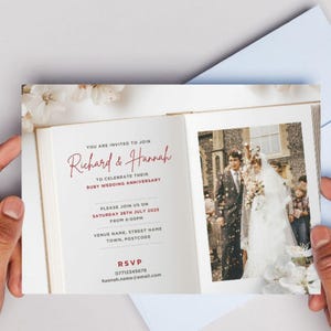May include: A wedding anniversary invitation with a photo of a couple in their wedding attire. The invitation is in the shape of an open book with white flowers on the cover. The text on the invitation reads "You are invited to join Richard & Hannah to celebrate their Ruby Wedding Anniversary. Please join us on Saturday 26th July 2025 from 6:00pm. Venue name, street name, town, postcode. RSVP 07712345678 hannak name remall.com."