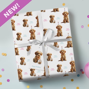 May include: Gift-wrapped present with a white ribbon and tag. The paper displays a repeating pattern of a brown puppy, a cupcake, and the words "Happy Birthday!". A purple banner in the corner reads "NEW!"