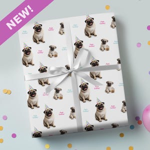 May include: White wrapping paper with a repeating pattern of pugs in party hats and cupcakes. The words "Happy Birthday!" are scattered across the design. A white ribbon is tied around the wrapped gift. The word "NEW!" is in a purple banner.