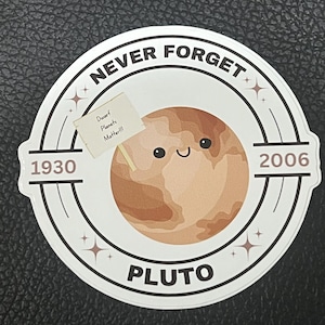 May include: A circular sticker featuring a cartoon Pluto with a smiling face. The sticker has the text "NEVER FORGET" around the top, with "1930" and "2006" on either side. A small sign reads "Dwarf Planets Matter!!!".