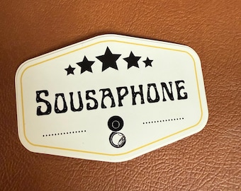 Könnte beinhalten: Ein weißer Aufkleber mit gelbem Rand und schwarzem Text, der "Sousaphone" lautet. Über dem Text befinden sich fünf schwarze Sterne. Unter dem Text befindet sich eine Schwarzweißillustration eines Sousaphons.