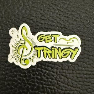 May include: A white sticker with a green musical note and the text "GET STRINGY" in green letters.