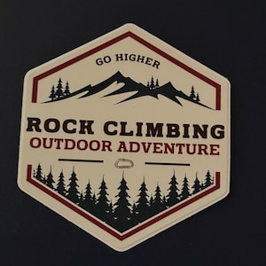 May include: A hexagonal sticker with a mountain and forest design. The sticker has the words "GO HIGHER" at the top and "ROCK CLIMBING OUTDOOR ADVENTURE" in the center. The sticker is white with a red border and dark brown text.