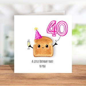May include: A square birthday card featuring a cartoon slice of toast with a party hat and holding a pink "40" balloon. The toast is also holding a glass of champagne. The text reads "A LITTLE BIRTHDAY TOAST TO YOU."
