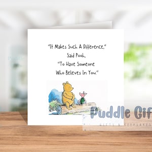 May include: A square greeting card with a quote from Winnie the Pooh. The card features an illustration of Pooh Bear and Piglet. The quote reads, "It Makes Such A Difference, Said Pooh, To Have Someone Who Believes In You."