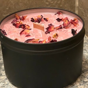 May include: A black candle jar with a pink wax top. The wax is filled with dried rose petals and clear crystals.