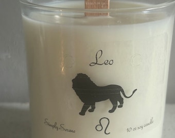 Puede incluir: Una vela de soja blanca con una silueta negra de un león y el texto "Leo" y "Simply Serene" en la parte delantera. La vela está en un frasco de vidrio transparente con una mecha de madera y está etiquetada como "10 oz soy candle".