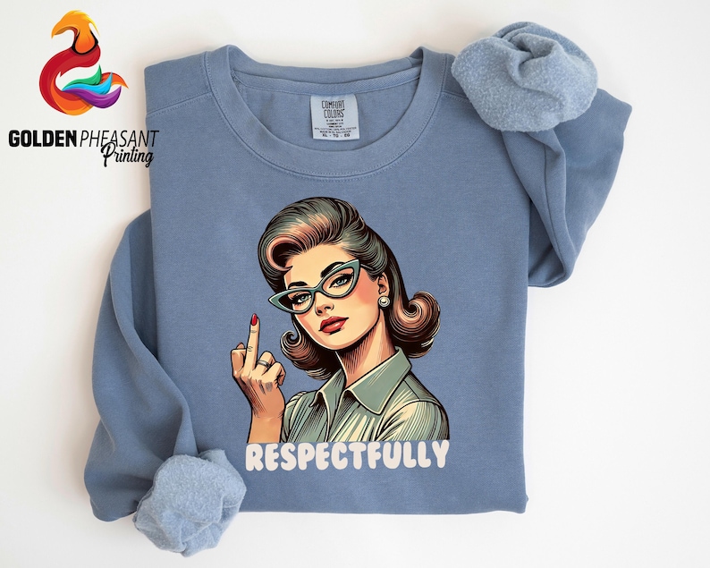 May include: A blue long-sleeve sweatshirt featuring a retro-style illustration of a woman wearing cat-eye glasses and a button-up shirt, giving the middle finger. The word "RESPECTFULLY" is printed below the illustration.