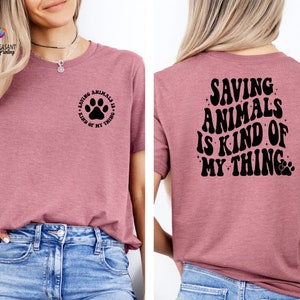 May include: A pink t-shirt with the text "Saving Animals is Kind of My Thing" on the back and a paw print with the text "Saving Animals is Kind of My Thing" on the front.