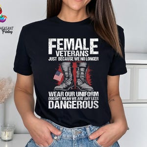 May include: Black t-shirt with a white graphic design featuring a pair of military boots and an American flag. The text reads "Female Veterans Just Because We No Longer Wear Our Uniform Doesn't Mean We Are Any Less Dangerous".