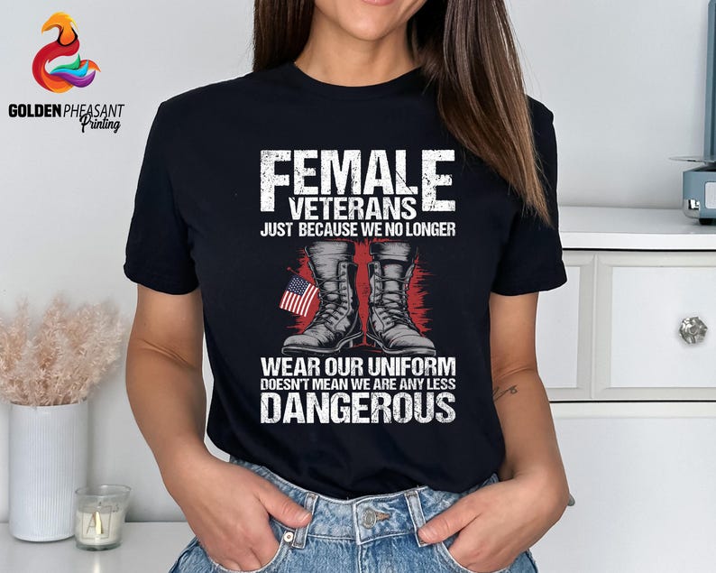 May include: Black t-shirt with a white graphic design featuring a pair of military boots and an American flag. The text reads "Female Veterans Just Because We No Longer Wear Our Uniform Doesn't Mean We Are Any Less Dangerous".