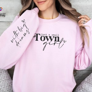 May include: Pink sweatshirt with the text "Just a small town girl" and "with big dreams" on the sleeve.