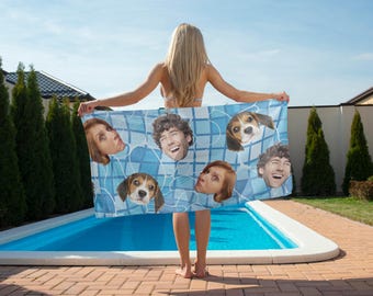 May include: A blue and white patterned beach towel featuring a grid design with faces and beagle dog faces. The towel is held up in front of a pool on a sunny day.