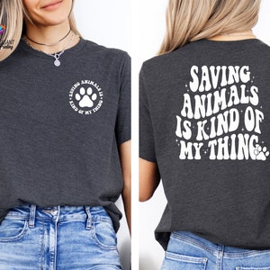 May include: A dark gray t-shirt with a white paw print and the text "Saving Animals is Kind of My Thing" on the front and the same text in a larger font on the back.