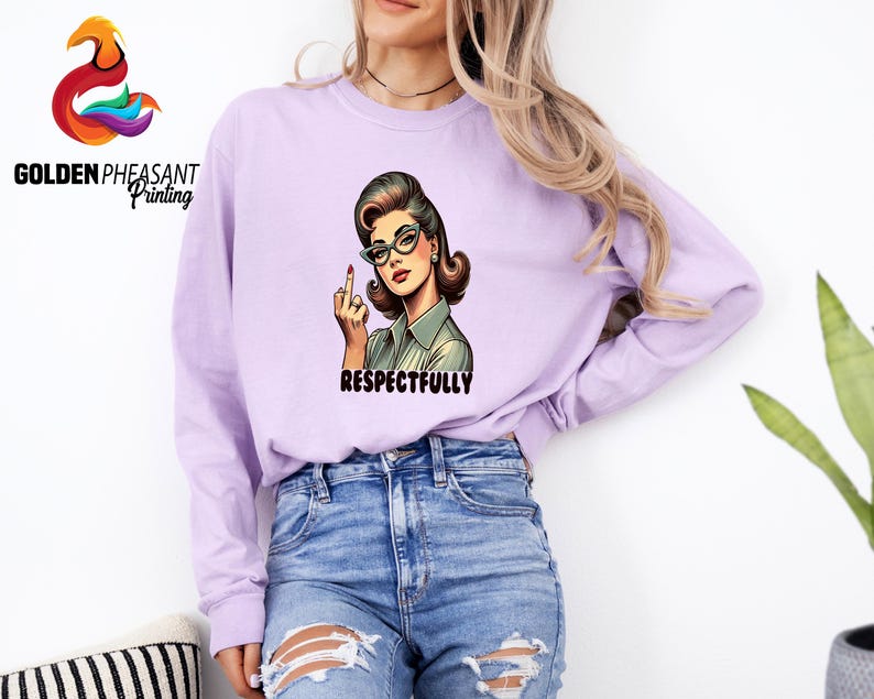 May include: A light purple long-sleeve sweatshirt featuring a retro illustration of a woman wearing glasses and giving the middle finger. The word "RESPECTFULLY" is printed below the illustration. The sweatshirt is paired with blue jeans.