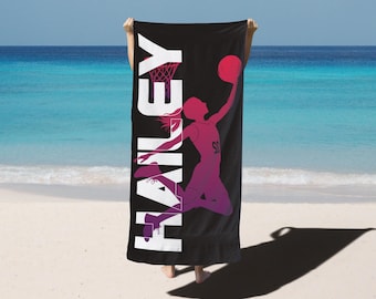 May include: Black beach towel featuring a basketball player silhouette in shades of pink and purple, with the name "HAILEY" in large white letters. The player is mid-jump, about to shoot the ball. The background is a beach with blue water and sky.