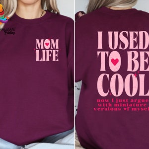 May include: Burgundy sweatshirt with pink text that reads "MOM LIFE" on the front and "I USED TO BE COOL now I just argue with miniature versions of myself" on the back.