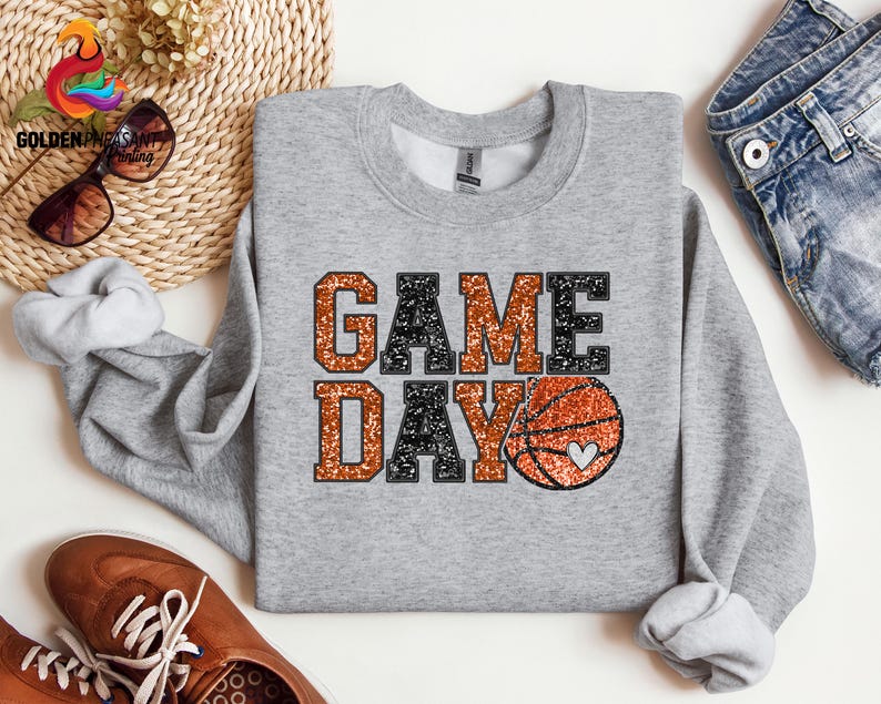 May include: A gray sweatshirt with the text "GAME DAY" in black and orange glitter. A basketball with a heart is in the middle of the text.