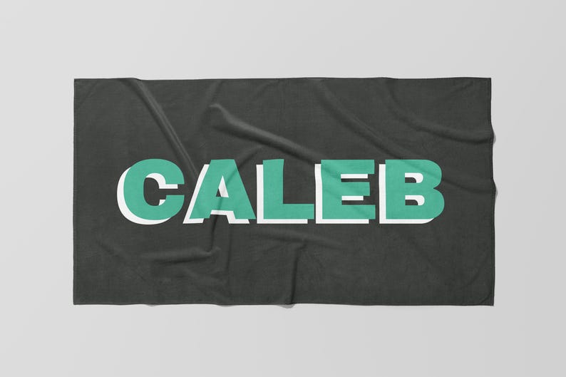 May include: A dark gray blanket with the name "CALEB" in large, block letters. The letters are teal with a white outline, creating a 3D effect. The blanket is folded and has a soft, textured appearance.