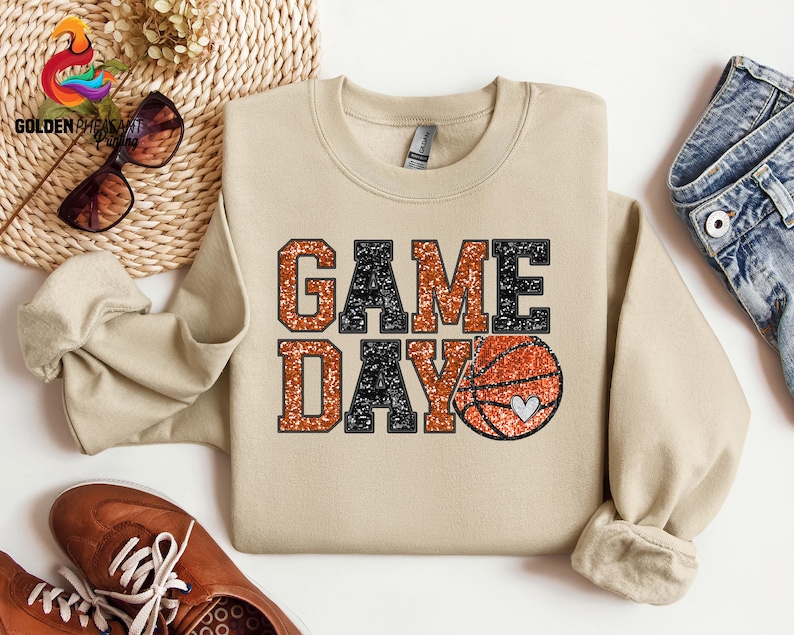 May include: A tan sweatshirt with the text "GAME DAY" in black and orange glitter lettering. A basketball with a small heart is next to the text.