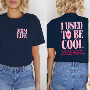 May include: Two navy blue t-shirts with pink text. The first shirt says "MOM LIFE" with a pink heart. The second shirt says "I USED TO BE COOL now I just argue with miniature versions of myself".
