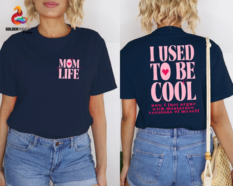 May include: Two navy blue t-shirts with pink text. The first shirt says "MOM LIFE" with a pink heart. The second shirt says "I USED TO BE COOL now I just argue with miniature versions of myself".