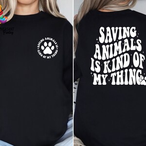 May include: Black sweatshirt with white text that reads "Saving Animals is Kind of My Thing" with a paw print.