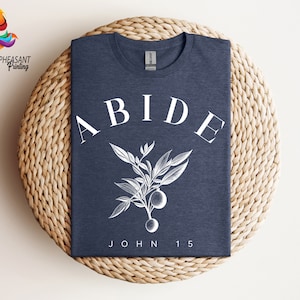 May include: A navy blue t-shirt with white text that reads "ABIDE" with a stylized branch and fruit design. The text "JOHN 15" is printed below the design.