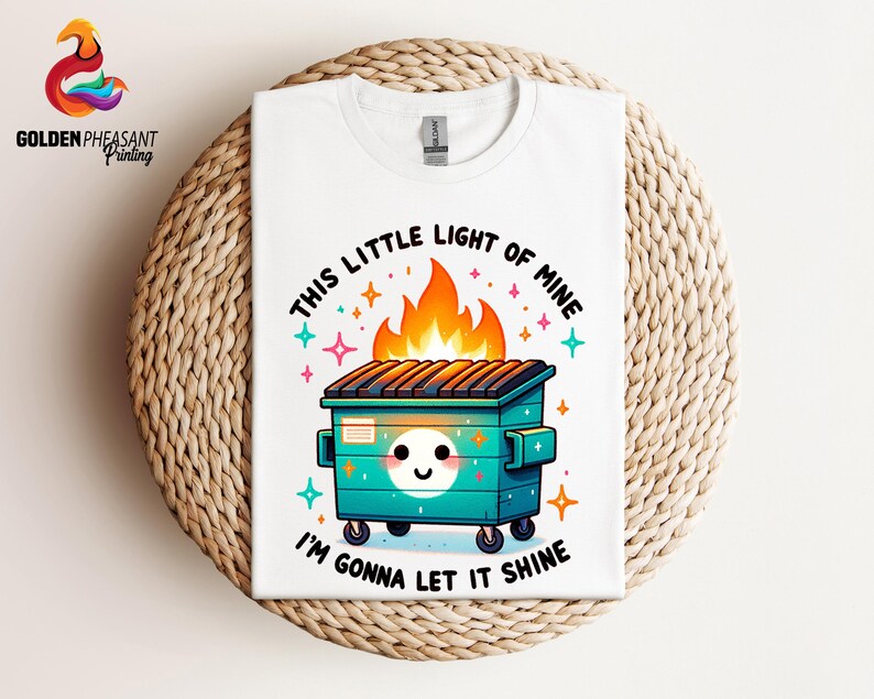 Pu&ograve; includere: Maglietta bianca con un cassonetto verde in fiamme con un viso sorridente e il testo "This little light of mine I'm gonna let it shine".