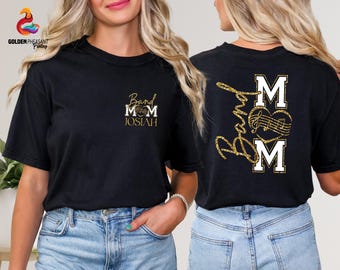 May include: Black t-shirt with gold glitter text and a musical note design. The front of the shirt says "Band Mom" with the name "Josiah" underneath. The back of the shirt says "Band Mom" with musical notes.