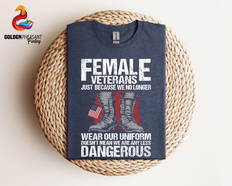 May include: A navy blue t-shirt with a white graphic design featuring a pair of military boots and an American flag. The text on the shirt reads "Female Veterans Just Because We No Longer Wear Our Uniform Doesn't Mean We Are Any Less Dangerous".